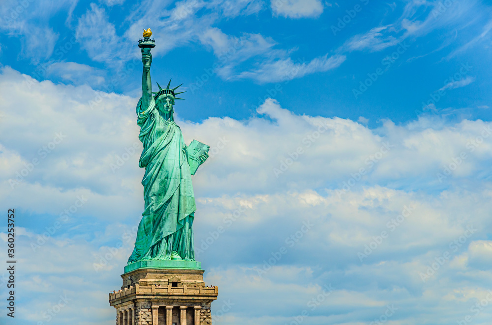 Fototapeta premium The Statue of Liberty designed by Alexandre Gustave Eiffel on a blue sky with white clouds background with 4th of July writing visible on Liberty Island in New York, USA in black and white