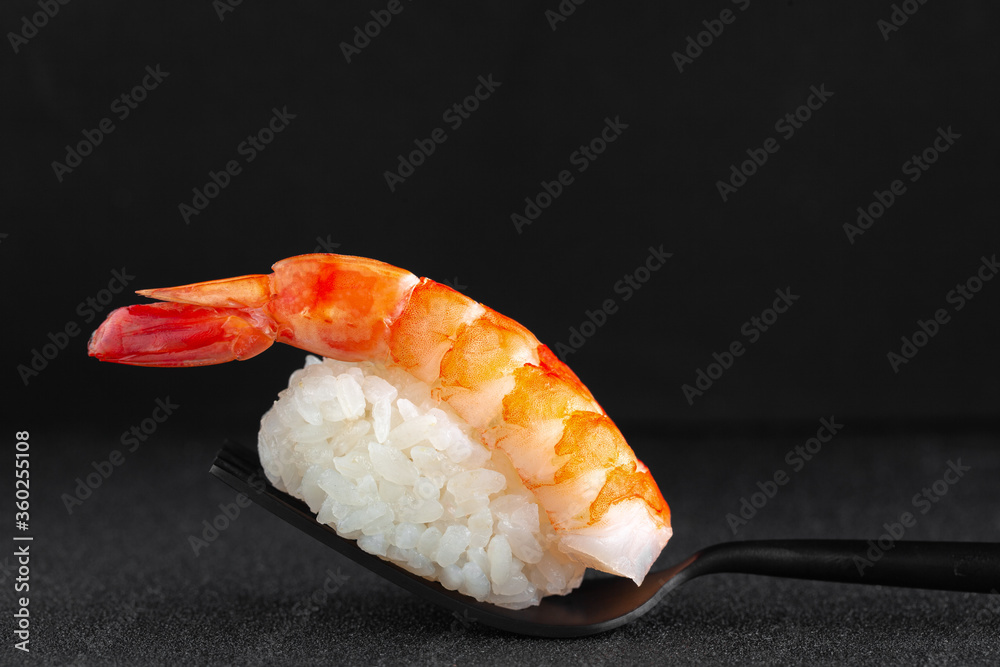 Close-up nigiri sushi with fresh shrimp on black fork on black background Close-up nigiri sushi with fresh shrimp on black fork on black background