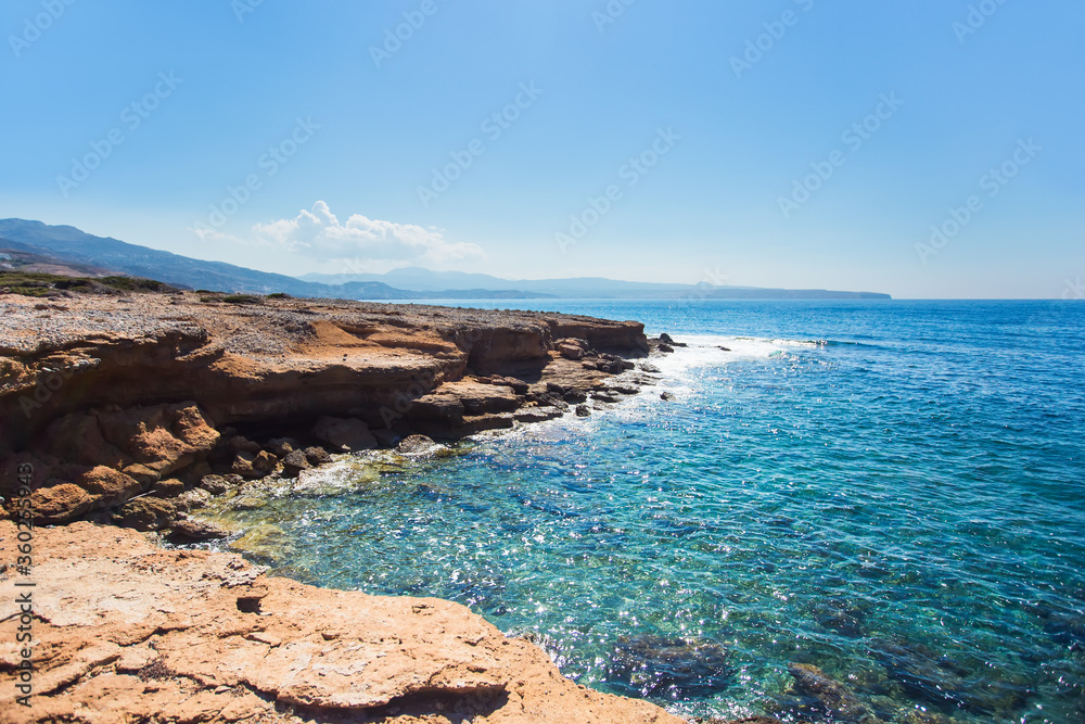 Cliff. Rocky coast of an island in Mediterranean sea.  Waves crash on rocks. Blue sky and sea.