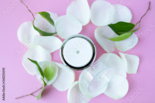 an open jar of cosmetic cream and white rose petals on a pink background. cosmetics with the concept of floral style. selective focus.