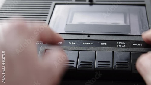 Insert white audio cassette into black cassette player and press play. Volume adjustment. Close-up shot