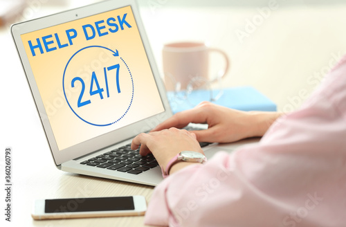 Woman using laptop at table indoors, closeup. Help desk service