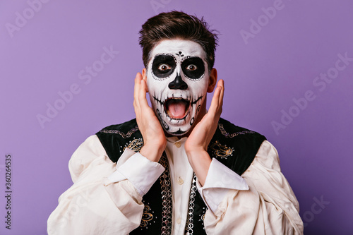 Shocked brown-eyed man screaming on purple background. Handsome male model in zombie costume expressing amazement in halloween.