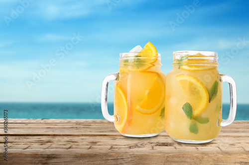 Mason jars with lemonade on wooden table near sea, space for text