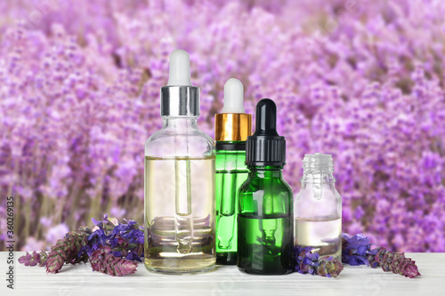 Bottles of essential oils and wildflowers on wooden table against blurred background