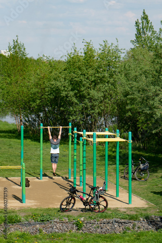 Athlete pulling up on the horizontal bar. Sports field for exercise in the park.