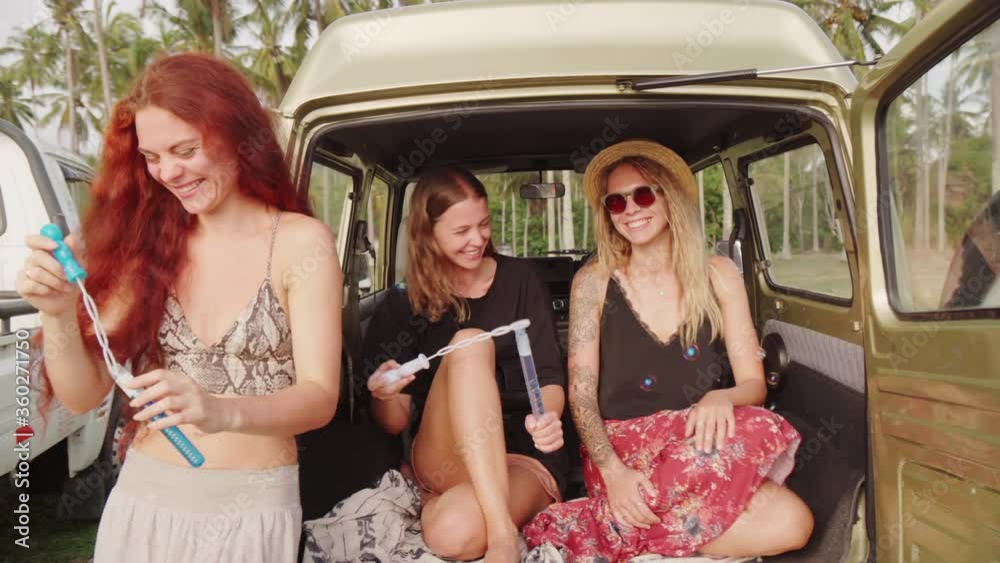 Handheld tracking shot of happy red-haired woman and her female friends blowing bubbles while relaxing on coast of Bali Handheld tracking shot of happy red-haired woman and her female friends blowing bubbles while relaxing on coast of Bali