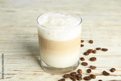 Delicious latte macchiato and coffee beans on white wooden table