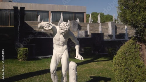 A white statue in the background of decorative fountain. Water flows over large artificial stones. Landscape design. 
