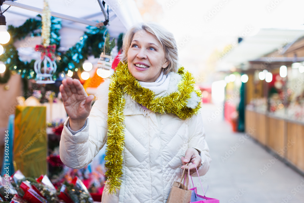 Positive mature female buying decoration at Christmas Fair