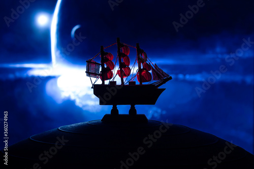 Beautiful boat toy over a blue balll with blurred blue deep universe scene at background. Travel, universe and space concept photo