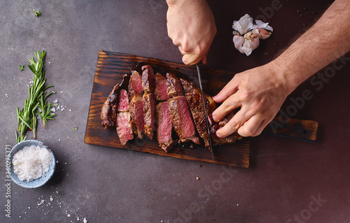 Male hands cutting cooked until medium ribeye steak on wooden cutting board.