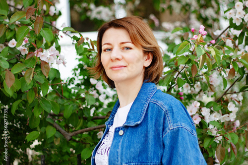 Beautiful brown haired woman with blue eyes in an Apple orchard sniffing blooming flowers on a spring day