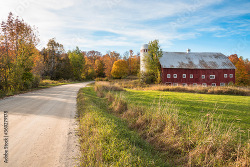 Red traditional barn with silo along an unpaved back road in the countryside of Vermont at sunset. Beautiful autumn colours. photo