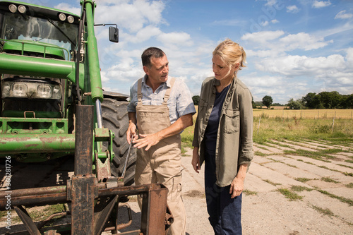 Man explaining woman while standing by agricultural machinery at farm