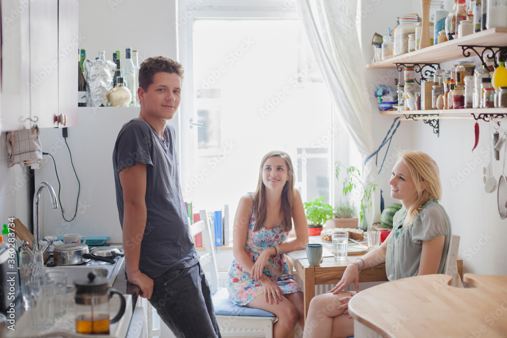 Portrait of handsome young man standing with female friends in kitchen at home Portrait of handsome young man standing with female friends in kitchen at home