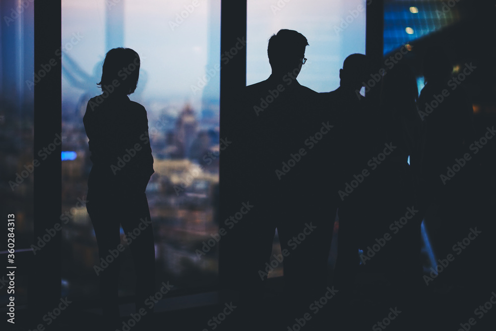 Silhouette of a group young purposeful financiers lead a conversation while standing in modern office interior, confident partners talking among themselves while resting after business meeting