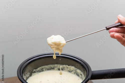 Close up of piece of bread being dipped in cheese fondue.