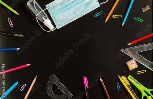 School supplies, face mask and hydroalcoholic gel on blackboard.