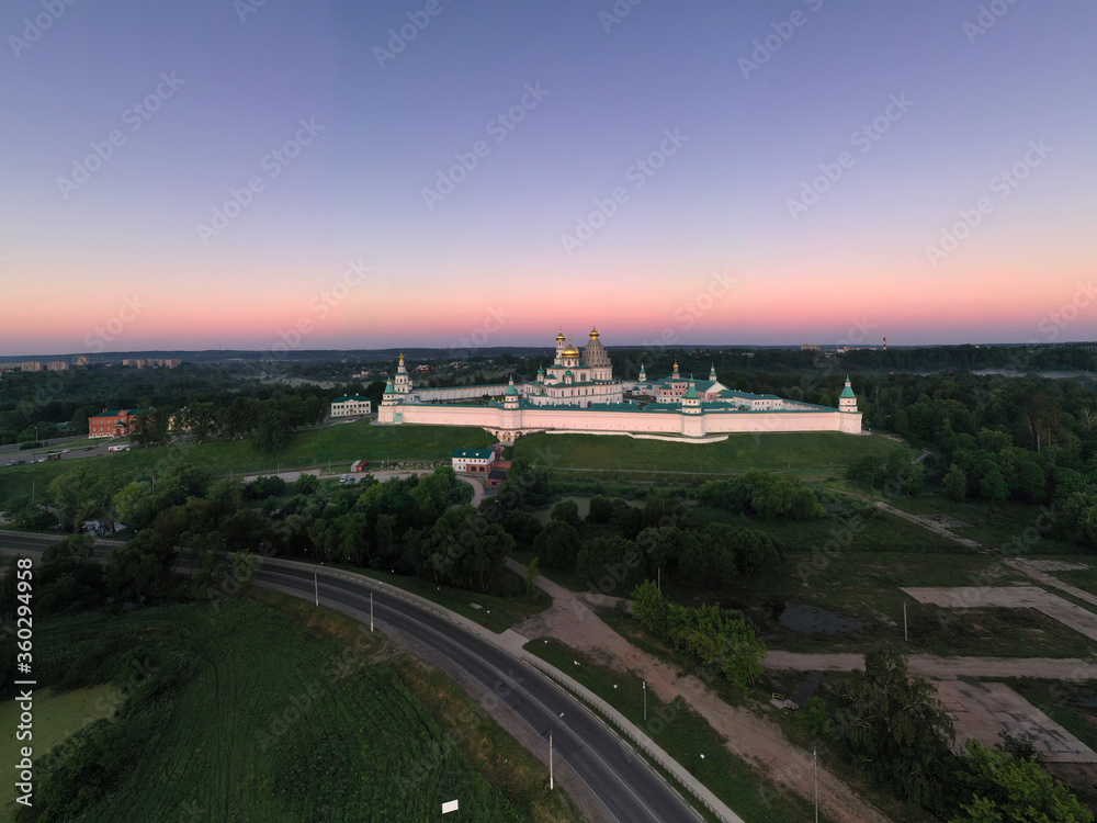 panoramic view of a white stone fortress on a green hill against the background of the rising sun, taken from a drone