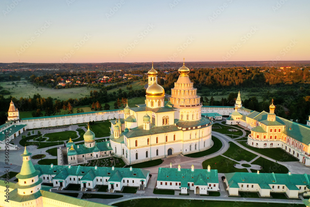 panoramic view of a white stone monastery on a green hill filmed from a drone at dawn
