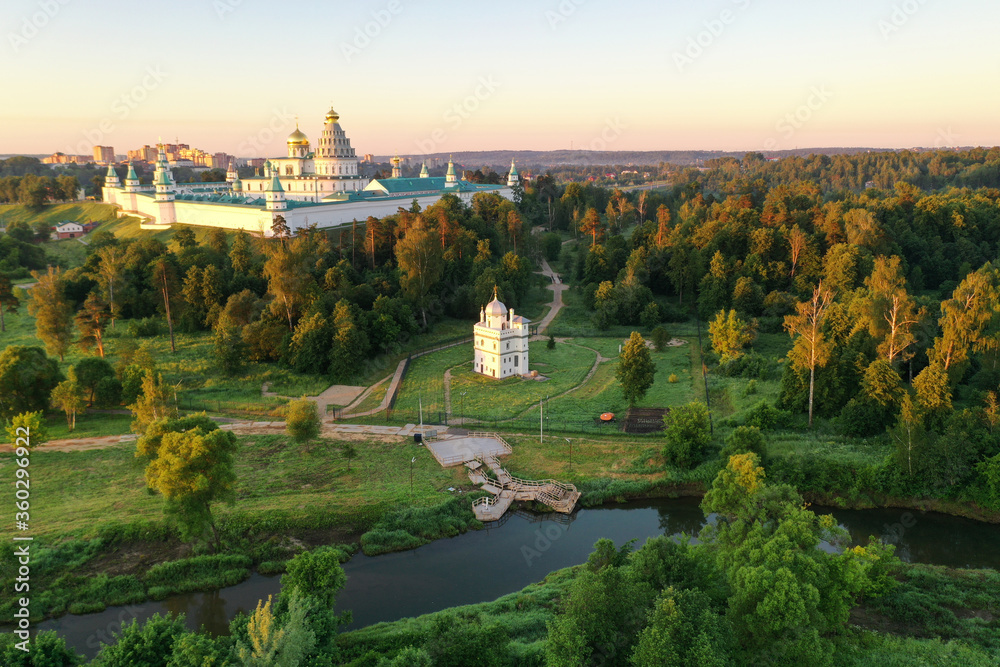 Naklejka premium panoramic view of a white stone monastery on a green hill filmed from a drone at dawn