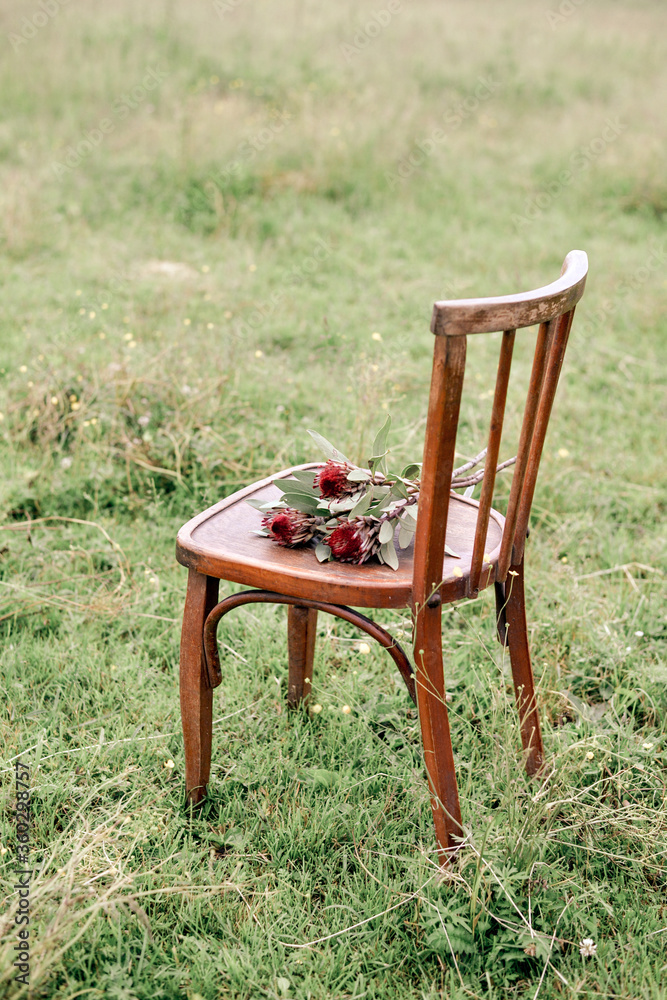 Exotic flowers laying on old wooden chair in front of green field Exotic flowers laying on old wooden chair in front of green field