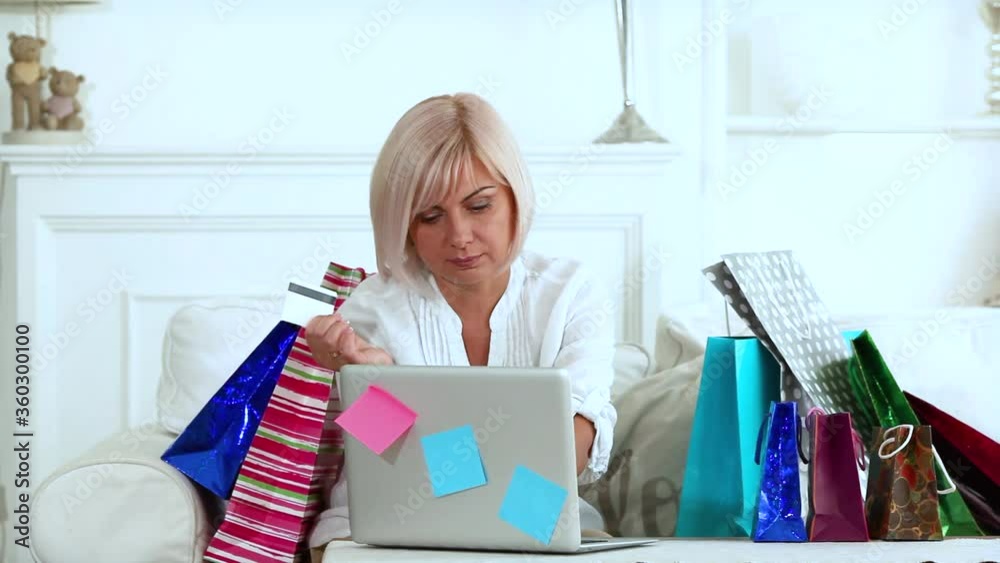 Woman doing online shopping at home sitting on a couch and using laptop. Female browsing internet goods. Woman doing online shopping at home sitting on a couch and using laptop. Female browsing internet goods.