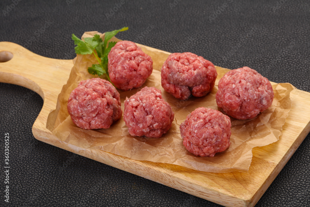 Raw meatball over wooden background