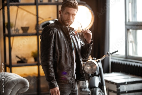 Perfect man. Young hipster in leather jacket standing in room.