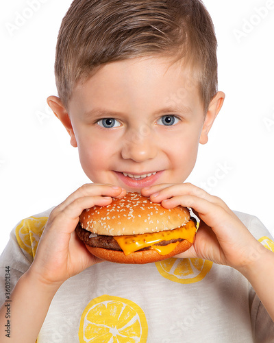 A child eats a cheeseburger. The boy looks at the Burger with an appetite. A beautiful European boy is going to eat fast food. Happy child. A hamburger snack. Favorite children's food.