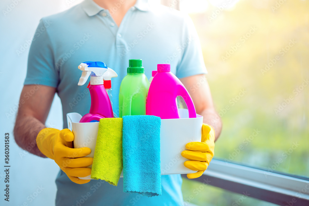 Мan in yellow rubber gloves holding a white plastic box with cleaning products and microfiber rags. Equipment for cleaning and supplies indoors, closeup. Closeup of man househusband Мan in yellow rubber gloves holding a white plastic box with cleaning products and microfiber rags. Equipment for cleaning and supplies indoors, closeup. Closeup of man househusband