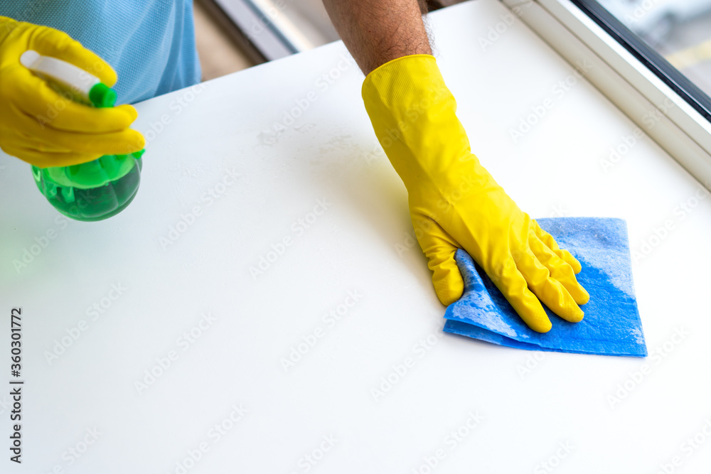 Professional cleaning. Top view. Close up of hands cleaning service man in rubber protective yellow gloves cleaning the white surface with a rag. Professional cleaning. Top view. Close up of hands cleaning service man in rubber protective yellow gloves cleaning the white surface with a rag.