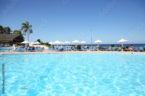 swimming pool with blue water and white umbrella in tropical resort. Vacation and travel concept