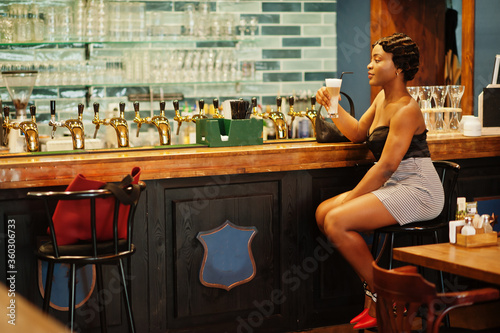 Portrait of african american woman, retro hairstyle posing at restaurant on bar counter with cup of latte.