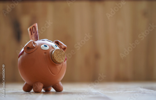 Clay brown piggy bank with a 10 euro bill in in it, space for text, wooden background