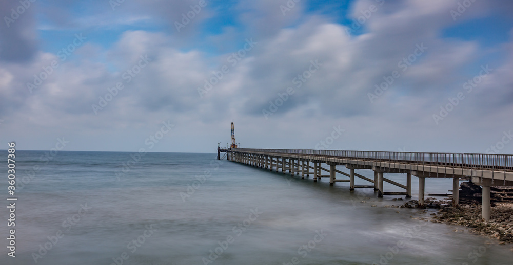 A horizontal shot of a wooden deck on a beautiful sandy beach under puffy clouds