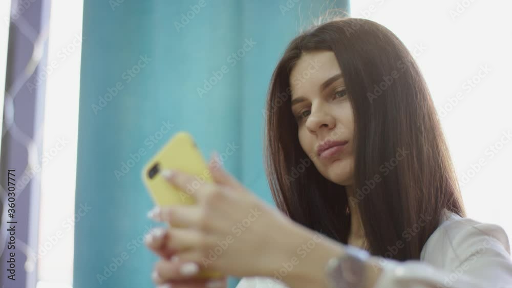 A side view slow motion close up of a young business woman taking a break during her work day and taking pictures of herself on her smartphone