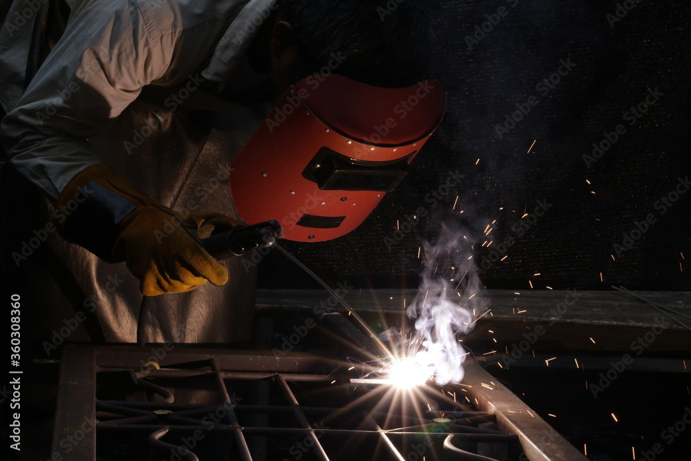 A Worker with an Iron Mask is Welding the Steel, we can see the Sparkle Fire and the Smoke A Worker with an Iron Mask is Welding the Steel, we can see the Sparkle Fire and the Smoke