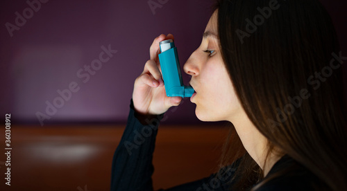 Woman inhaling a blue asthma inhaler at home. photo