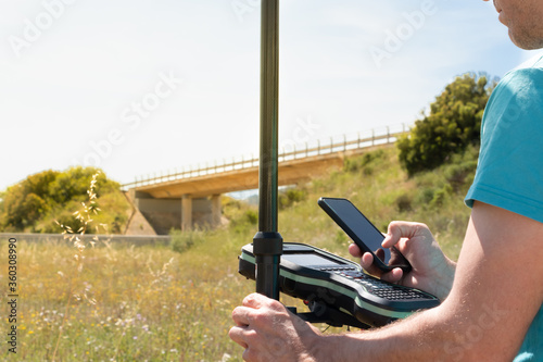 Land surveyor with a GPS instrument, checking data with his smartphone