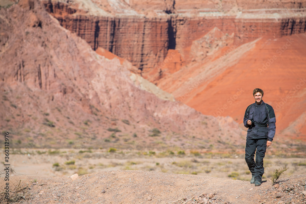 Man in motorcycle gear, standing in front of red sandstone formations