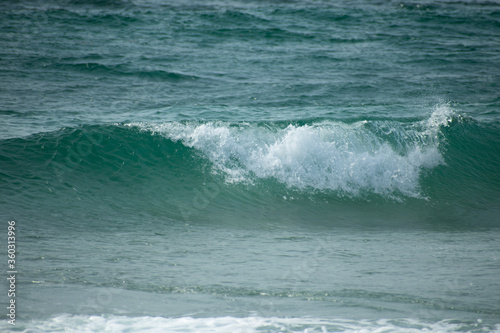 Small cresting wave in the Atlantic Ocean on the coast. Blue green ocean waves with sea foam and salt water spray. Beach travel photos.