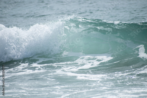 Small cresting wave in the Atlantic Ocean on the coast. Blue green ocean waves with sea foam and salt water spray. Beach travel photos.