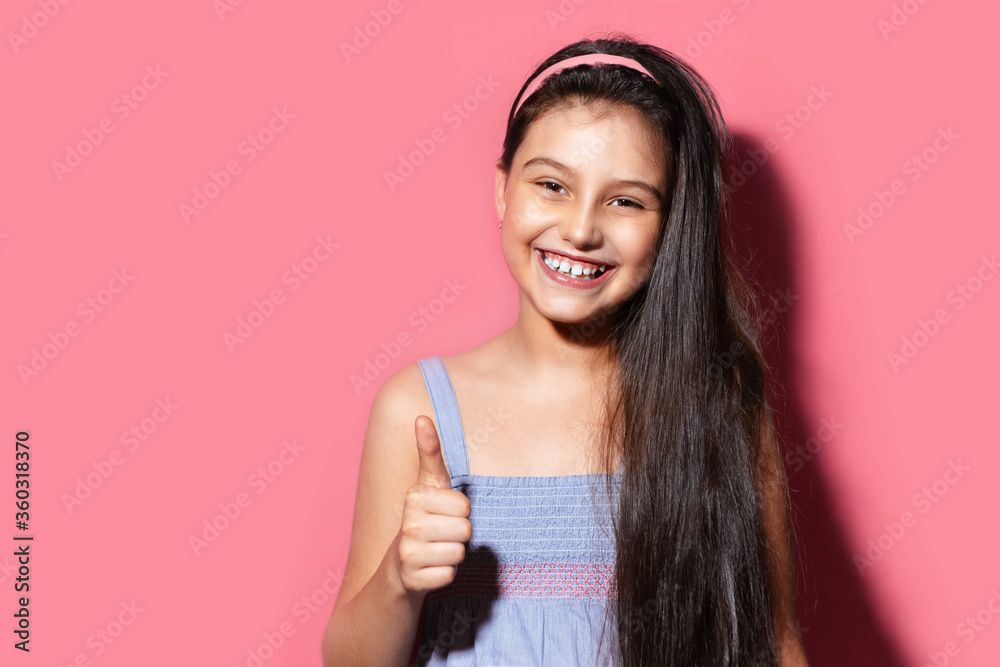 Studio portrait of happy teenage girl showing thumbs up on background of pastel pink color with copy space.