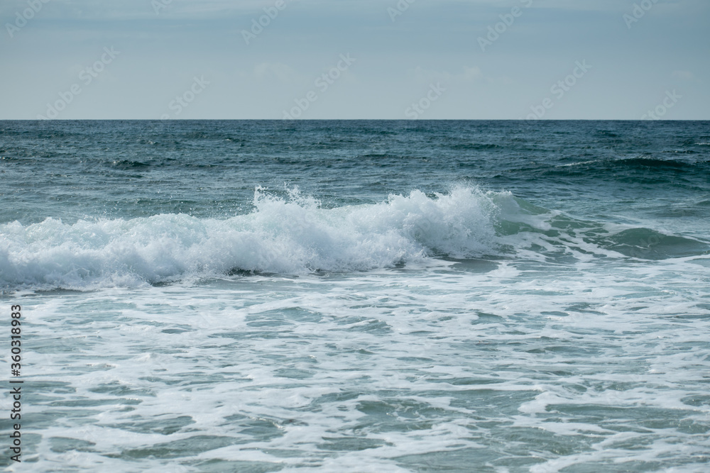Small cresting wave in the Atlantic Ocean on the coast. Blue green ocean waves with sea foam and salt water spray. Beach travel photos. Small cresting wave in the Atlantic Ocean on the coast. Blue green ocean waves with sea foam and salt water spray. Beach travel photos.
