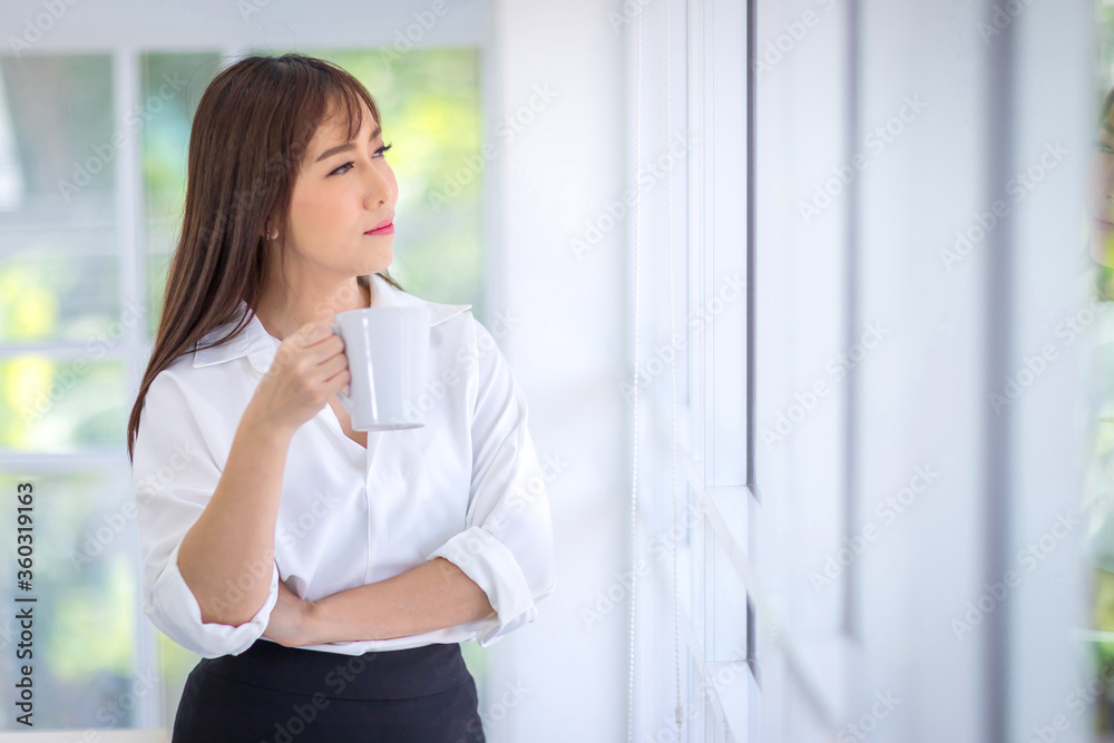 Beautiful Asian woman with long hair Wearing a white shirt standing, holding a white coffee cup and smile. Drink coffee concept. Beautiful Asian woman with long hair Wearing a white shirt standing, holding a white coffee cup and smile. Drink coffee concept.