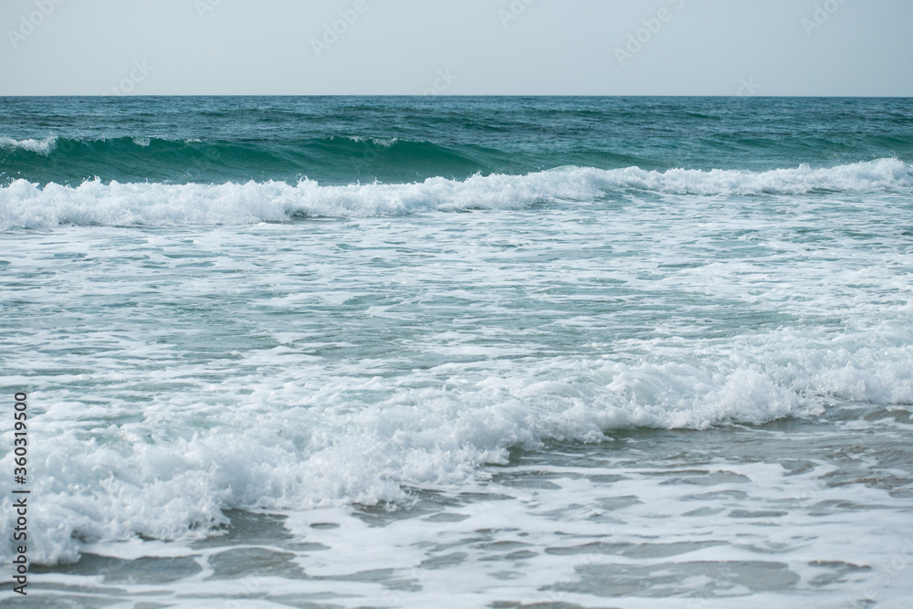 Small cresting wave in the Atlantic Ocean on the coast. Blue green ocean waves with sea foam and salt water spray. Beach travel photos.