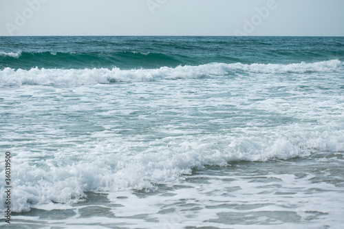 Small cresting wave in the Atlantic Ocean on the coast. Blue green ocean waves with sea foam and salt water spray. Beach travel photos.