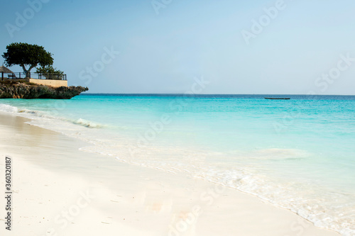 Clean white sand beach with turquoise water . Tropical island background. Small waves crushing on the beach. Clean empty white sand beach on Zanzibar. Rock on the beach 